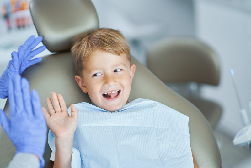 A child sitting in a dentist chair with hands raised, looking anxious